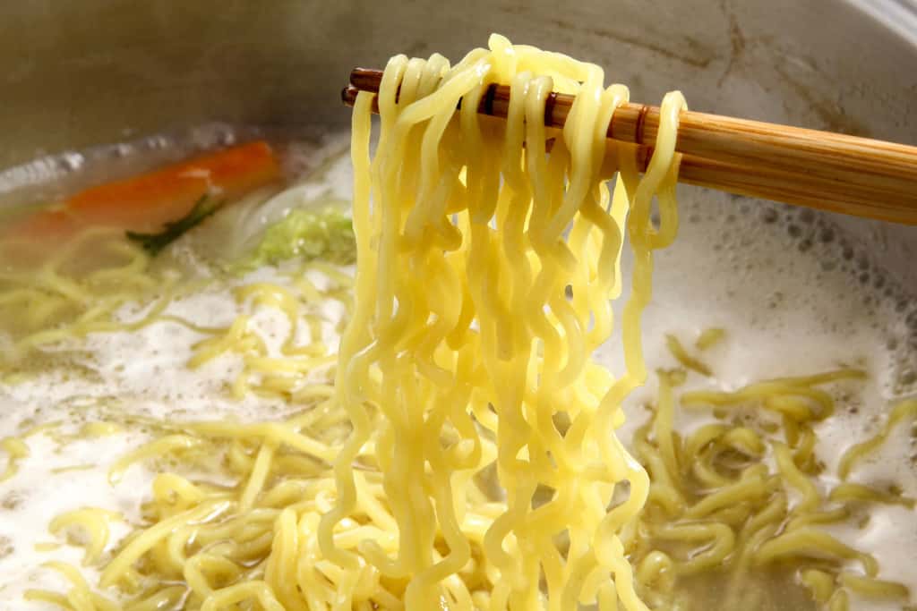水炊きスープで煮込んだラーメン、ラーメンの麺を箸で持ち上げる