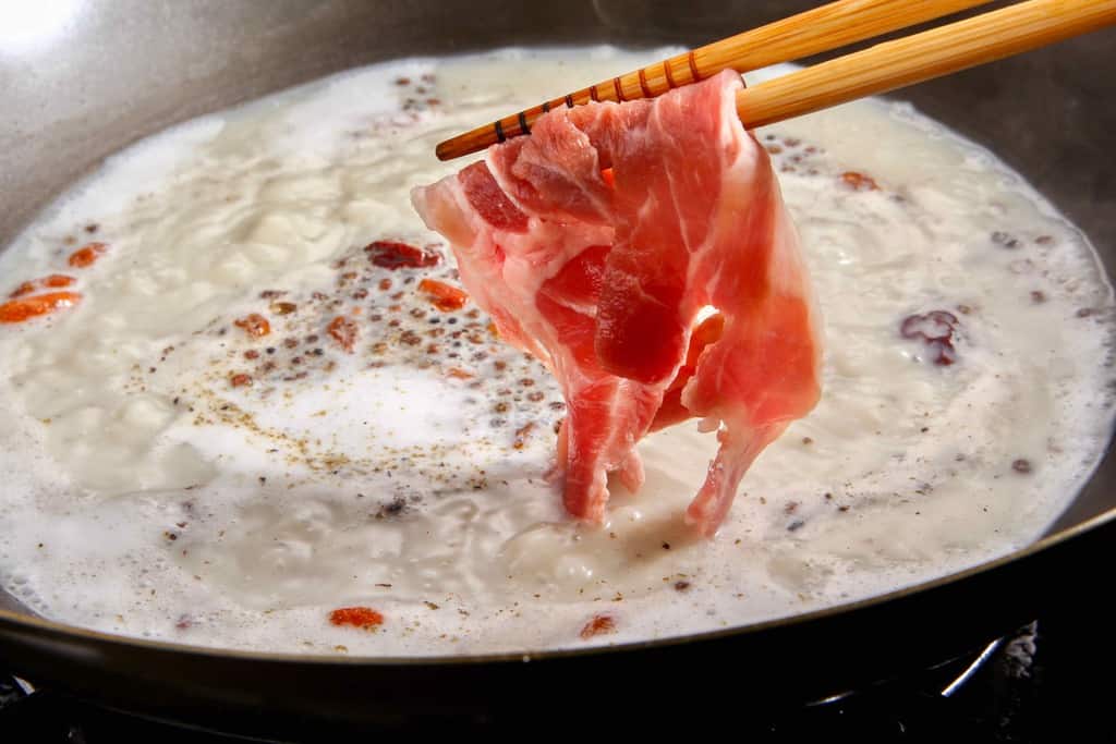 中華鍋の中の煮立った白湯スープにラム肉を入れる