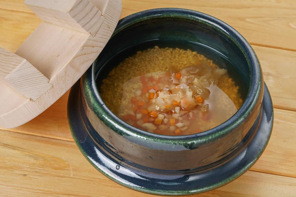 土鍋の中の米と調味液に野菜を加える、炊き込みご飯