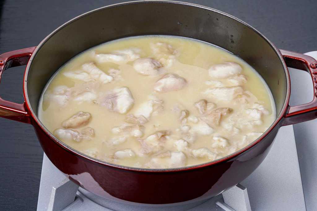 コンロの上の鍋にもつ鍋スープを入れて牛モツ（小腸）を入れる、スープとモツが入ったストウブ鍋