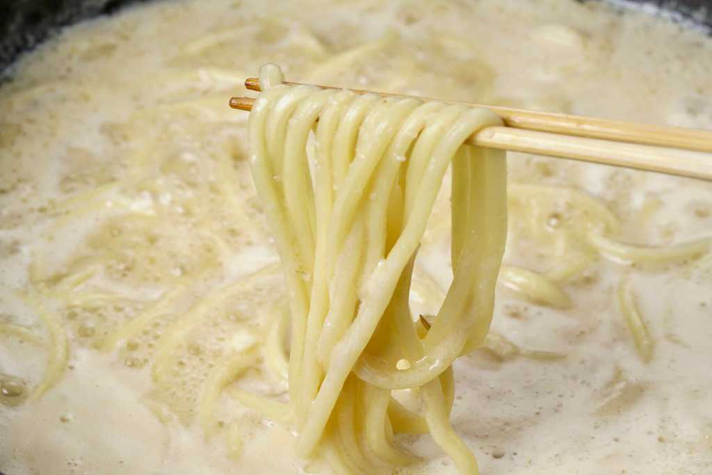 もつ鍋のしめのちゃんぽん麺を箸で持ち上げる、モツ鍋スープとチャンポン麺