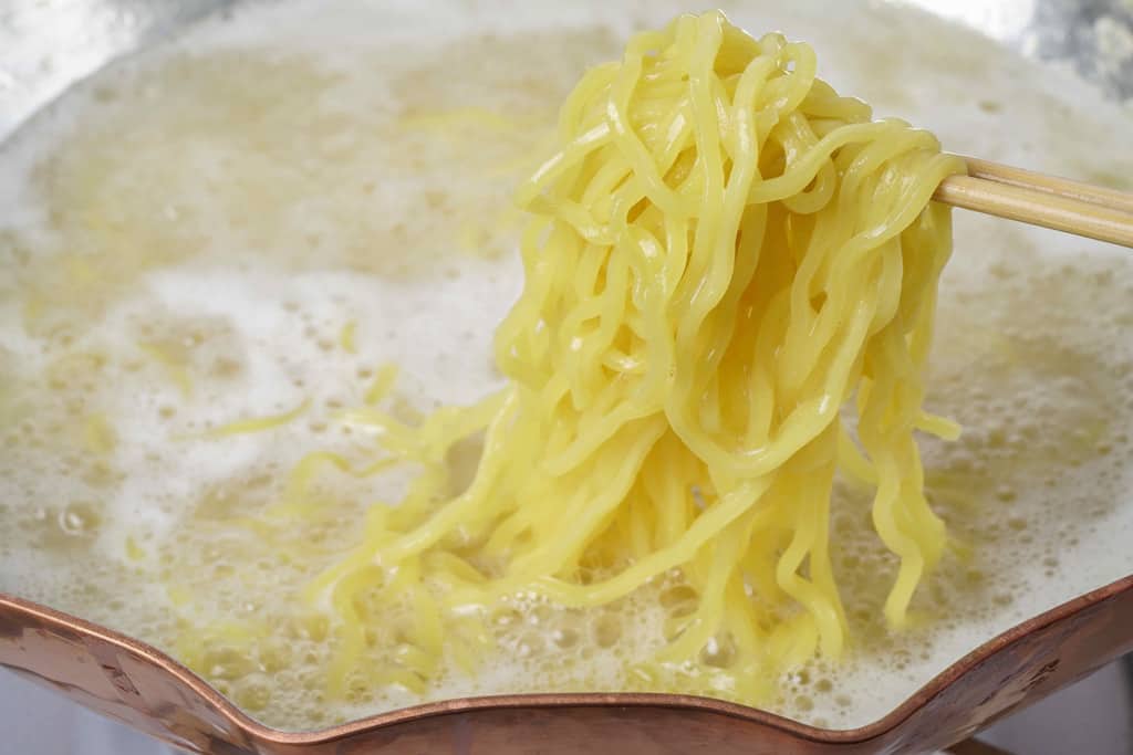 銅鍋の中で沸騰する水炊きスープにラーメンを入れる
