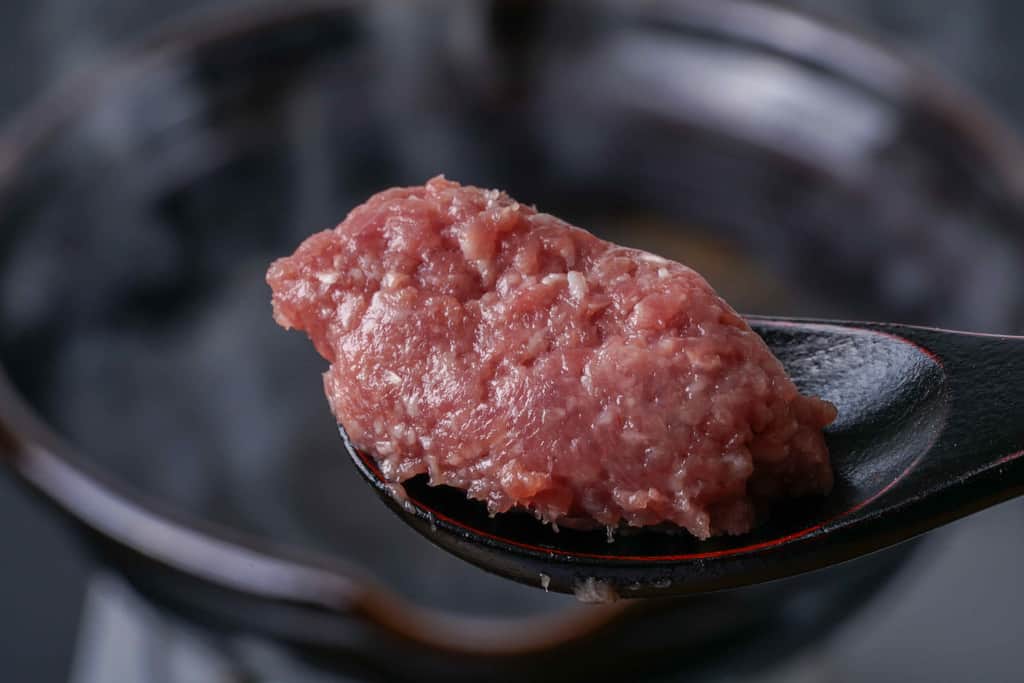 煮立った土鍋の中のスープにひと口大にした合鴨ミンチを入れる、レンゲの上の倭鴨のミンチ肉