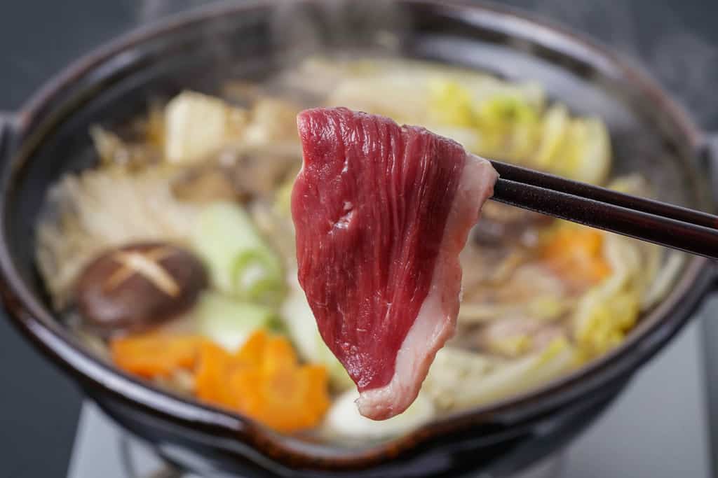 煮立った鍋に合鴨ロース肉を入れる、箸でつまんだ鴨重の倭鴨ロース肉