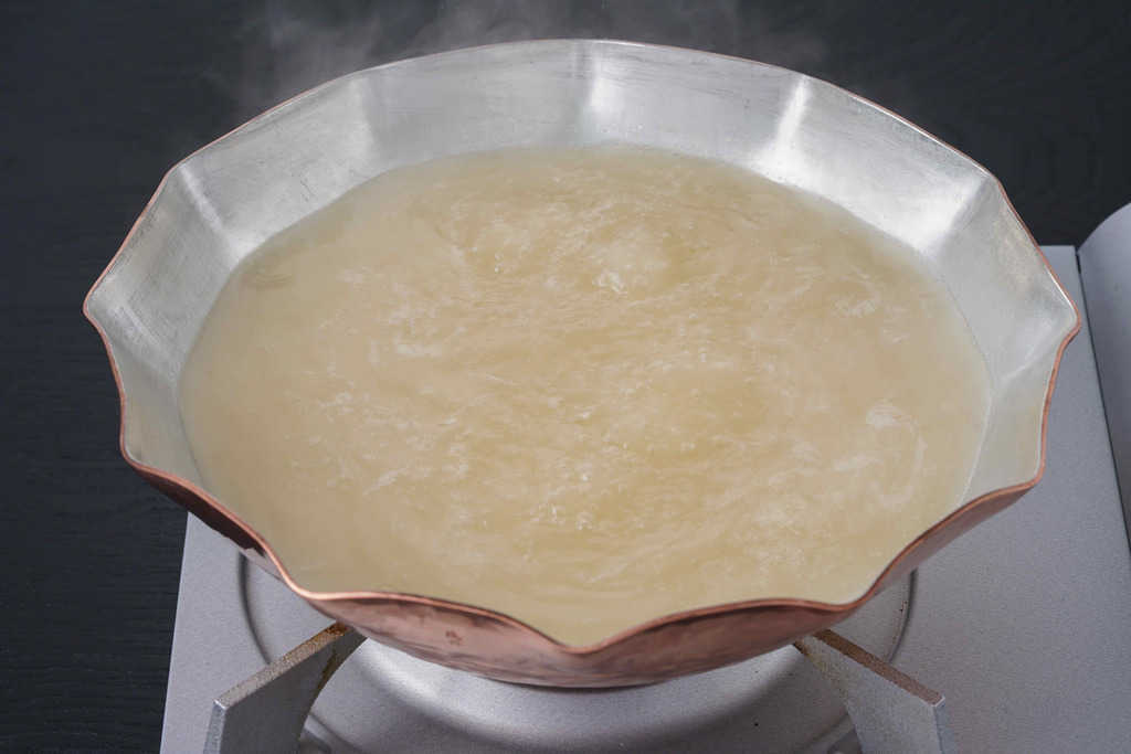 銅鍋の中で煮立っている三和の純鶏名古屋コーチンの水炊きスープ