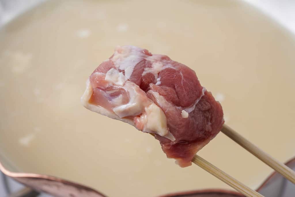 銅鍋の中で煮立っている水炊きスープに名古屋コーチンのモモ肉を入れる