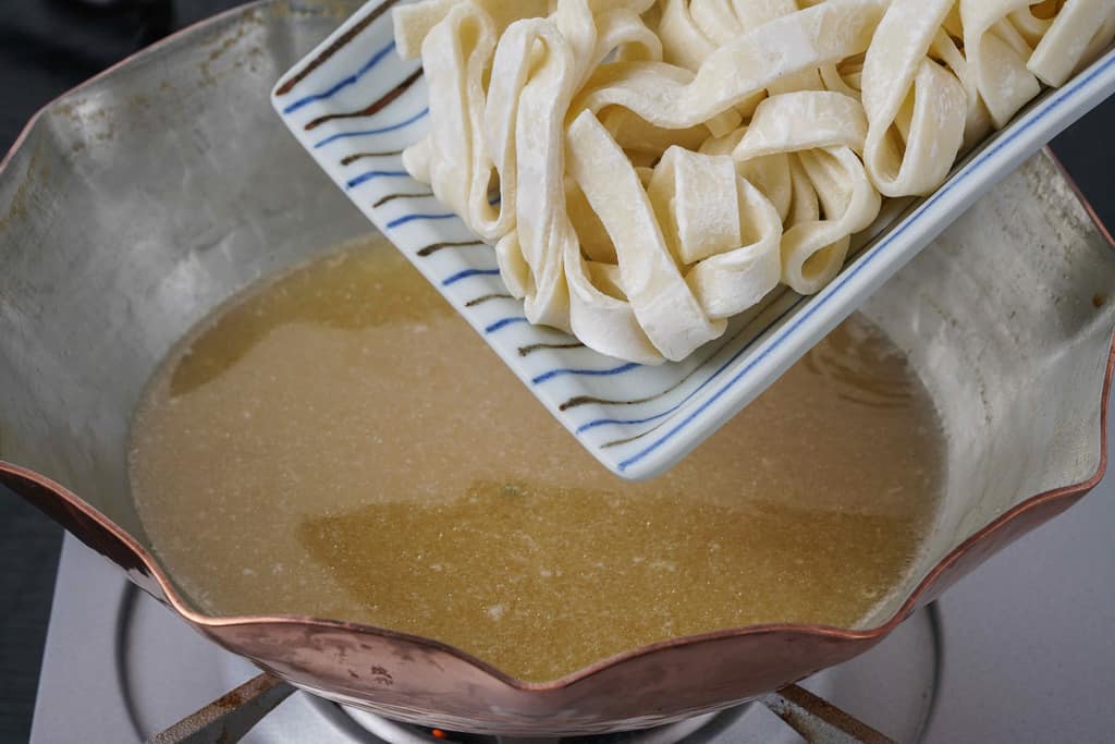 銅鍋の中の水炊きスープにきしめんを入れる