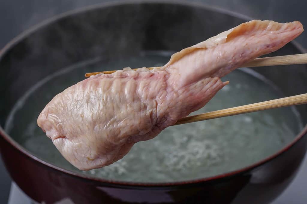 staub鍋の中で煮たった鶏ガラスープに手羽餃子を入れる、ストウブ鍋を背後に手羽餃子を箸で持つ